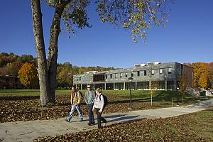 Three students walk down path in front of MacFarlane Center with fall colors on trees in background