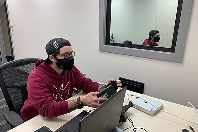 A student holds eyetracking equipment at a desk with a computer
