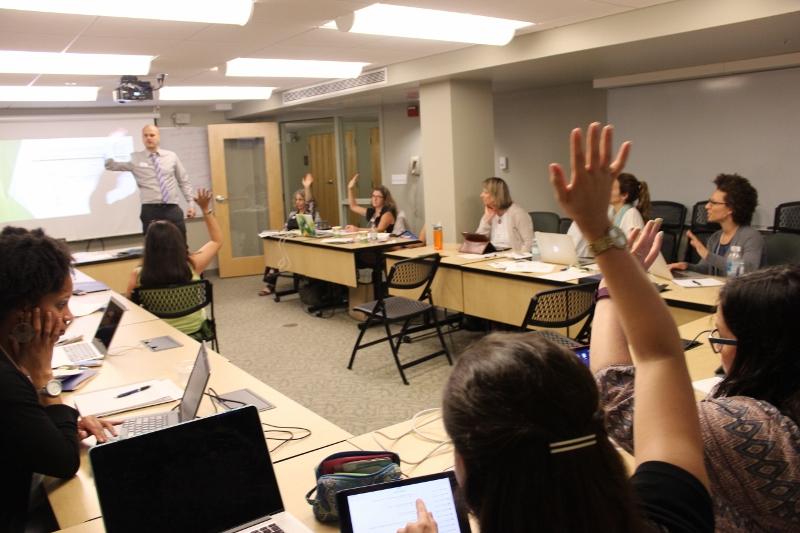 在地标学院的教室里，当LCIRT的主讲人围着桌子向学生讲话时，前排的参与者举手